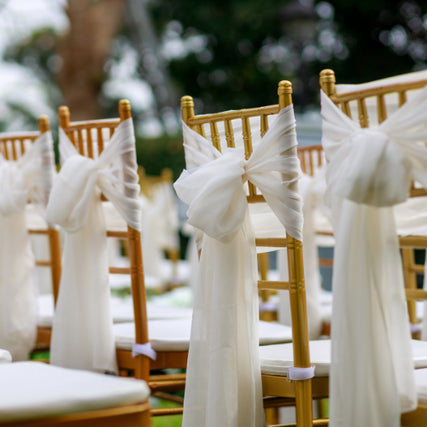 Party & Event RentalsGold chairs with white linen ribbons tied to the back of them.